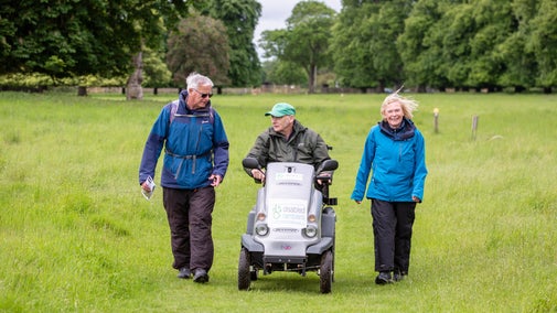 Three ramblers, the middle one on a mobility scooter, come towards the camera